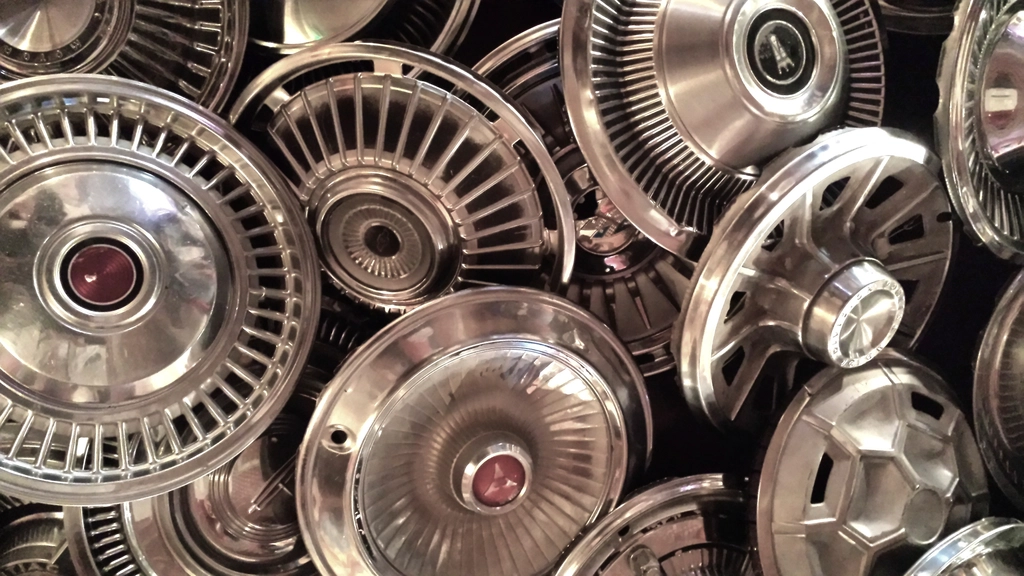 A collection of used chrome wheel covers and vintage car parts arranged for appraisal